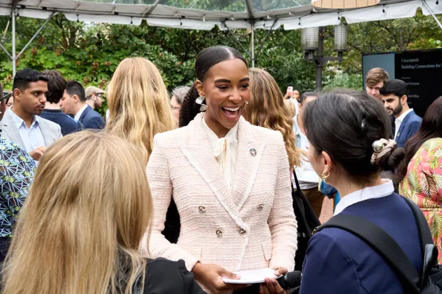 A Sisters founder laughing mid-conversation at an outdoor summit reception, notes in hand