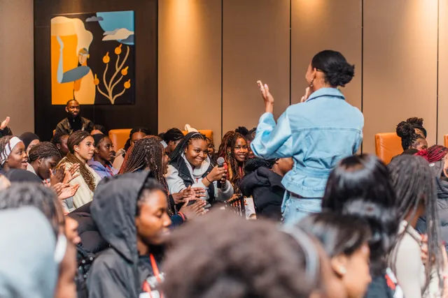 A girl in a packed room holding a microphone to ask a question while a Sisters founder listens